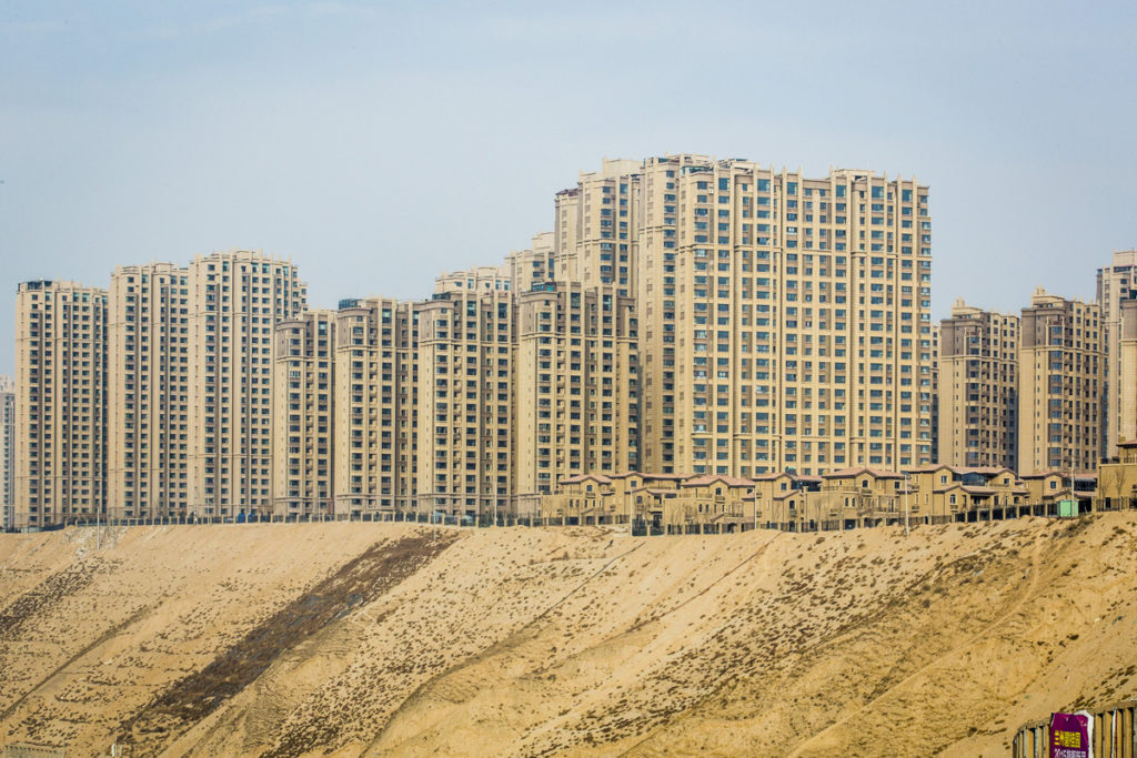 Située sur l’ancienne Route de la Soie, au Nord-Ouest de la Chine, Lanzhou, capitale de la province du Gansu, suffoque.
Construite au milieu de terres arides et désertiques, à 1600 mètres d'altitude sur pas moins de 20 km le long du fleuve Jaune (Huang He), Lanzhou est le plus important centre industriel du Nord-0uest chinois depuis les années 50. Elle compte aujourd’hui parmi les villes les plus polluées de Chine.
Coupée en deux par le Fleuve Jaune et entourée de montagnes, avec ses quelques deux millions d’habitants, Lanzhou ne peut plus grandir et poursuivre son développement économique. La densité d’habitants au Km 2 est en effet la même qu’à Pékin…sauf que nous sommes dans l’Ouest qui représente 56% du territoire chinois sur lequel vit seulement 11% de sa population. L’espace à conquérir est donc encore immense.
Le projet de déplacer la population de l’Est chinois vers l’Ouest pourrait devenir bien réel au travers de ces deux projets d’urbanisation en cours: Lanzhou New Area - pole commercial et ville résidentielle à 70 km au nord de Lanzhou initié en 2010 - et Bi Gui Yuan, future nouvelle ville à l’allure orwellienne à moins de 5 km du centre de Lanzhou dont les travaux ont commencé en 2012.
Mais, nous sommes en zone désertique, un environnement naturellement hostile à l’installation de l’homme, et les montagnes de loess (terre jaune argileuse caractéristique de la Chine du Nord) constituent l’essentiel du paysage. Aussi, pour parvenir à faire sortir de terre ces dizaines de forêts d’immeubles et ces routes qui n’en finissent pas de partir toujours plus loin dans les terres sablonneuses, des centaines de montagnes ont été arasées, donnant à ces projets des accents herculéens d’autant plus fous que leurs décideurs n’ont pas tenu compte de l’avis des experts mettant en garde contre le manque de ressources naturelles sur ces terres arides et les conséquences négatives au niveau environnemental: déséquilibre de l’écosystème et de la biodiversité, érosion des sols, poussières de sables venant s’ajouter à la pollution de l’air de Lanzhou…sans compter les problèmes d’irrigation et les projets de dérivation mis en oeuvre pour y remédier…..

Qu’importe ! Pour les autorités locales et les investisseurs, l’enjeu est d’attirer les futurs acheteurs en leur vendant le rêve occidental d’une vie meilleure dans des espaces verts et des habitats écologiques. Face à ces projets et investissements titanesques, 
villages paysans et terres agricoles ne pèsent pas lourds puisqu’ils disparaissent petit à petit à coups de pelleteuses en contrepartie de dédommagements financiers. 
La paix sociale est ainsi préservée. Après avoir accepté d’abandonner leur terre et, le plus souvent leur maison, les paysans sont indemnisés par le gouvernement et relogés gratuitement dans de nouveaux villages ou appartements. Les plus âgés touchent une pension et certains des plus jeunes deviennent ouvriers…dans le bâtiment…A suivre